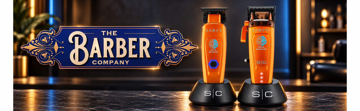 StyleCraft Saber 2 Professional Hair Clipper – Limited Edition Orange , set against a dark bar counter with a blurred bar background and a decorative 'The Barber Company' sign on the left.